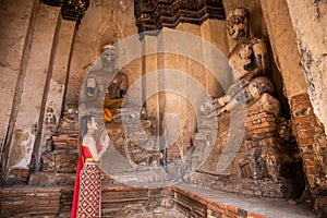 Young woman dressed in traditional red Thai dress and golden ornaments stands Worship Buddha statues greeting in the ancient site