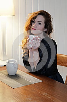 Young woman in dressing gown drinking cup of coffee sitting at kitchen table