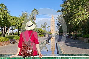 Young woman dressing in red with hat looking the mosque of Koutoubia in Marrakesh