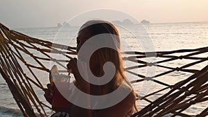 Young Woman Drink Cocktail Swinging in Hammock at Sunset