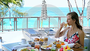 Young woman drink orange juice sitting in cafe in resort on summer vacation. Female tourist eat buffet breakfast or
