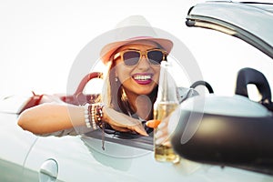 Young woman drinking a beer and looking the sunset. She is sitting in a sportive car.