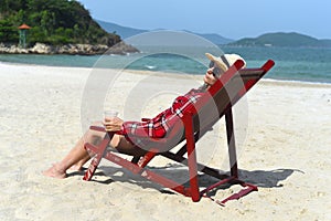 Young woman drinking beer and sitting on deck chair at beach in Nha Trang