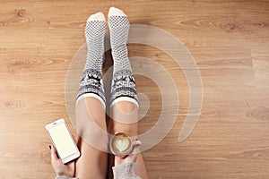 Young woman drinking cappuccino coffee and sitting on the wooden floor. Close up of female hands holding cup of coffee, sitting on