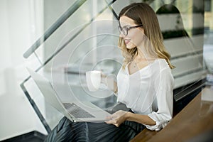 Young woman drinking coffe and working on laptop in office