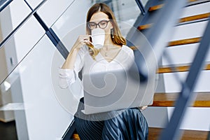 Young woman drinking coffe and working on laptop in office