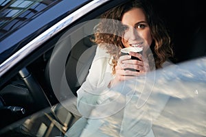Young woman drinking coffee in car interior.