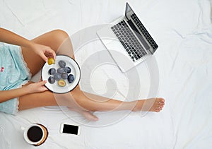 Young woman drinking coffee at home in her bed and checking her