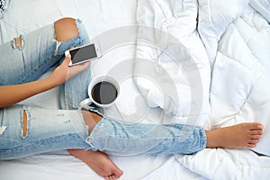 Young woman drinking coffee at home in her bed and checking her