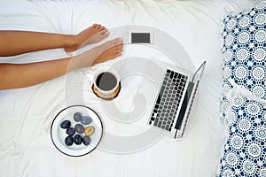 Young woman drinking coffee at home in her bed and checking her