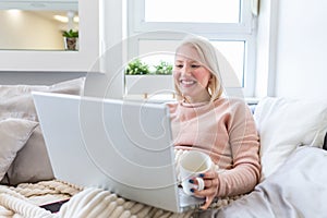 Young woman drinking coffee at home in her bed and checking her laptop. Beautiful young woman drinking coffee at home in her bed