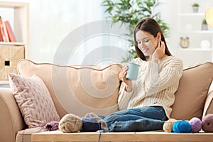 Young woman drinking coffee after knitting at home