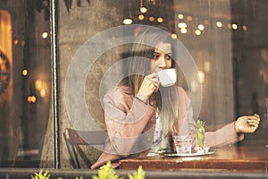 Young woman drinking coffee sitting indoor in urban cafe. Pretty cute girl and holding cup of coffee