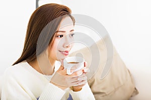 Young woman drinking coffee and sitting on sofa