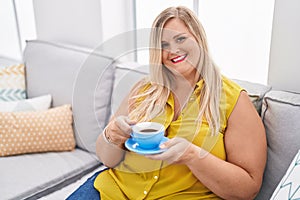 Young woman drinking coffee sitting on sofa at home