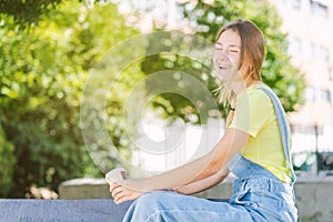 Young woman drinking coffee, sunbathing and laughing in the park. New normality, lifestyle, beauty, park