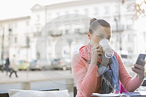 Young woman drinking coffee while using cell phone at sidewalk cafe