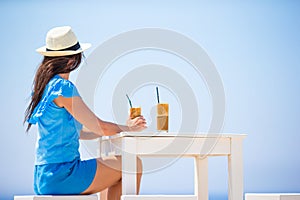 Young woman drinking cold coffee enjoying sea view. Beautiful woman relax during exotic vacation on the beach enjoying