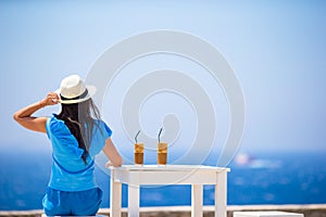 Young woman drinking cold coffee enjoying sea view. Beautiful woman relax during exotic vacation on the beach enjoying