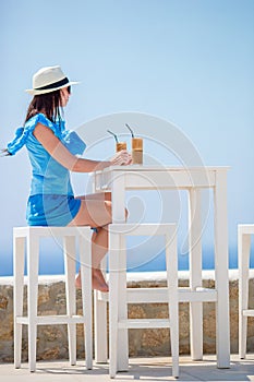 Young girl drinking cold coffee enjoying sea view. Beautiful woman relax during exotic vacation on the beach enjoying