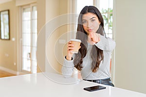 Young woman drinking a cup of coffee at home pointing with finger to the camera and to you, hand sign, positive and confident