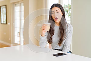 Young woman drinking a cup of coffee at home scared in shock with a surprise face, afraid and excited with fear expression