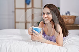 Young woman drinking cup of coffee lying on bed at bedroom