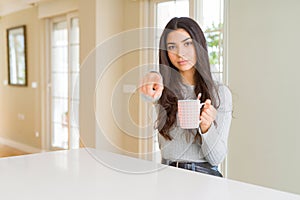 Young woman drinking a cup of coffee pointing with finger to the camera and to you, hand sign, positive and confident gesture from