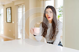 Young woman drinking a cup of coffee scared in shock with a surprise face, afraid and excited with fear expression