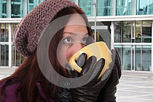 Young woman drinking cup of tea in winter outdoors in town