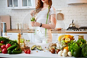 Young woman drinking fresh water with cucumber, lemon and leaves of mint from glass in the kitchen. Healthy Lifestyle and Eating.