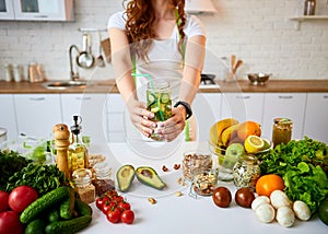 Young woman drinking fresh water with cucumber, lemon and leaves of mint from glass in the kitchen. Healthy Lifestyle and Eating.