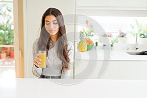 Young woman drinking a glass of fresh orange juice with a confident expression on smart face thinking serious