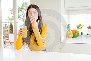 Young woman drinking a glass of fresh orange juice cover mouth with hand shocked with shame for mistake, expression of fear,