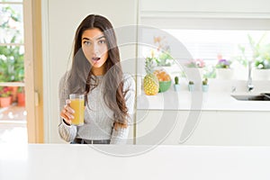 Young woman drinking a glass of fresh orange juice scared in shock with a surprise face, afraid and excited with fear expression
