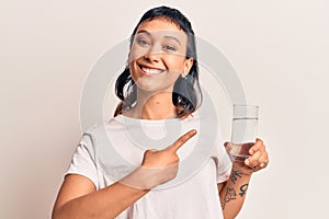 Young woman drinking glass of water smiling happy pointing with hand and finger