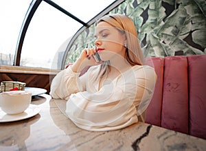 Young woman drinking hot coffee and talking on phone in sidewalk cafe