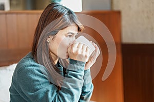 young woman drinking hot tea in winter, asian female enjoying a cup of coffee at home in the morning