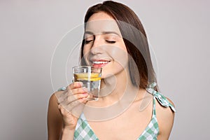 Young woman drinking lemon water on background