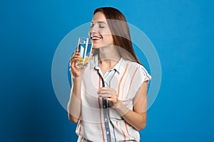 Young woman drinking lemon water on blue background