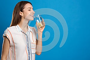 Young woman drinking lemon water on blue background. Space for text