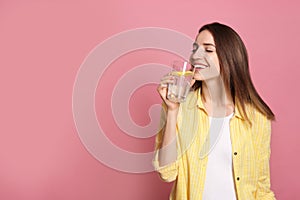 Young woman drinking lemon water on pink background. Space for text