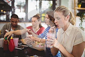 Young woman drinking milkshake with friends at cafe