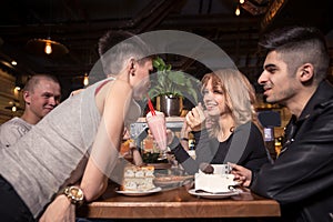 Young woman drinking milkshake while sitting with friends at cafe