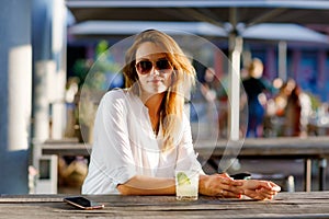 Young woman drinking mojito cocktail at cafe terrace at hot summer day. Beautiful businesswoman enjoying warm evening at