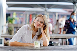 Young woman drinking mojito cocktail at cafe terrace at hot summer day. Beautiful businesswoman enjoying warm evening at