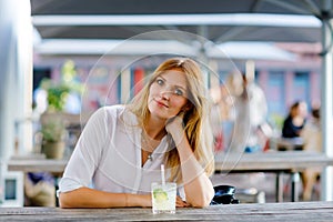 Young woman drinking mojito cocktail at cafe terrace at hot summer day. Beautiful businesswoman enjoying warm evening at