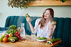 Young woman drinking smoothie and fresh water in the beautiful interior with green flowers on the background and fresh fruits and