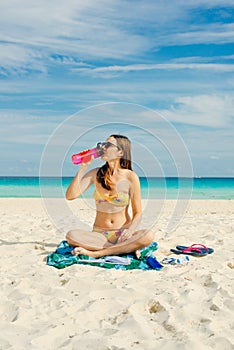 Young woman drinking sparkling water from transparent bottle on the beach, cancun