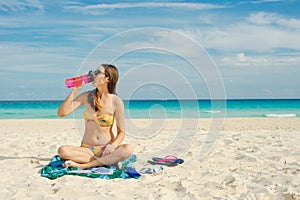 Young woman drinking sparkling water from transparent bottle on the beach, cancun